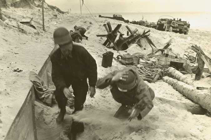 photograph of Fred Gerretson on a beachfront, taking cover from enemy fire.